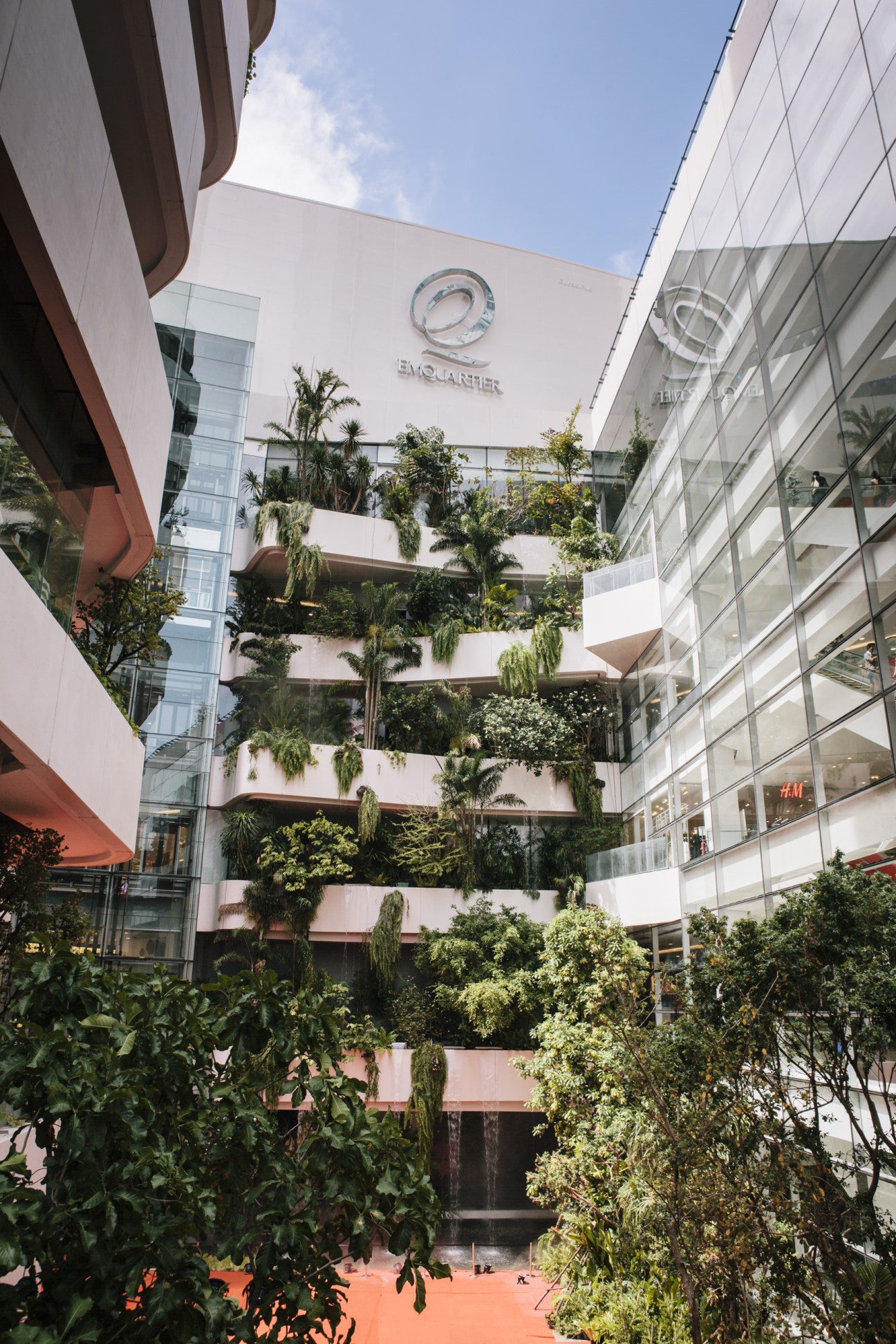 EmQuartier's exterior facade with cascading greenery across tiered terraces and the EmQuartier logo visible above.