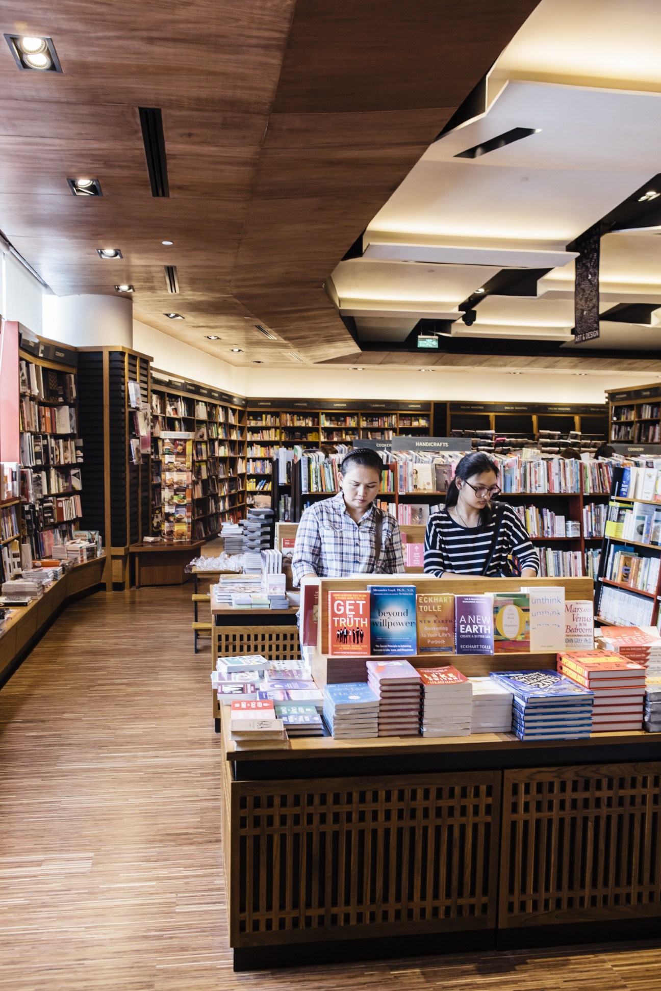 Two staff members work behind the counter of Kinokuniya bookstore with shelves of books and modern ceiling design.
