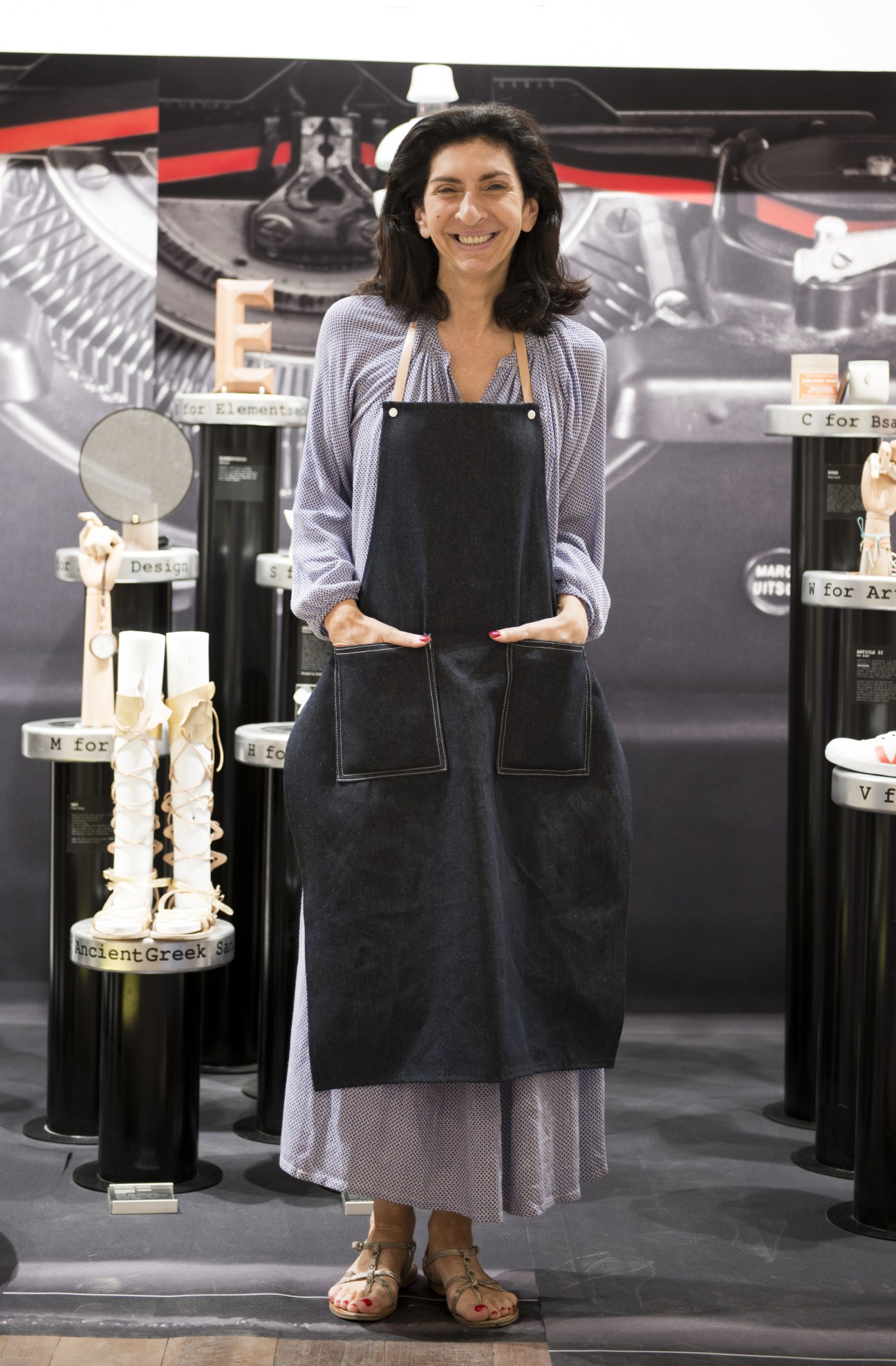 Shop assistant smiling in denim apron at EmQuartier retail store with display cases behind