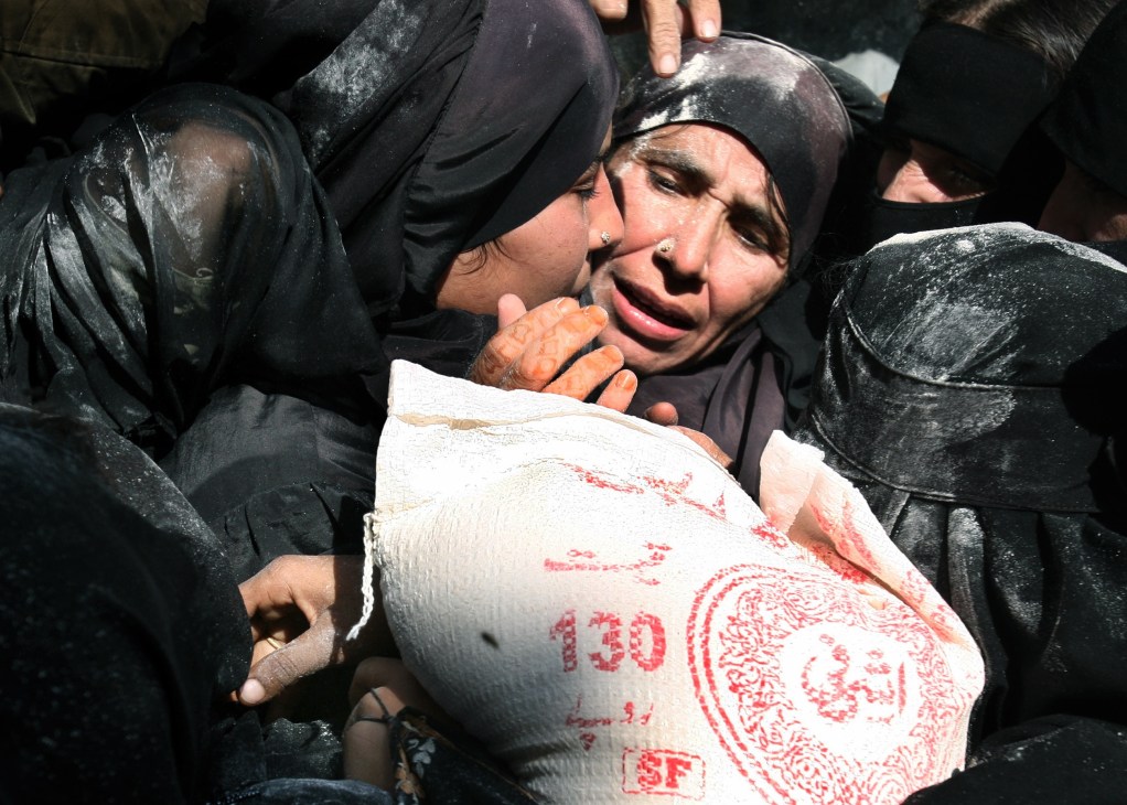 Women in black clothing jostle to obtain government-subsidised sacks of flour marked with red stamps.
