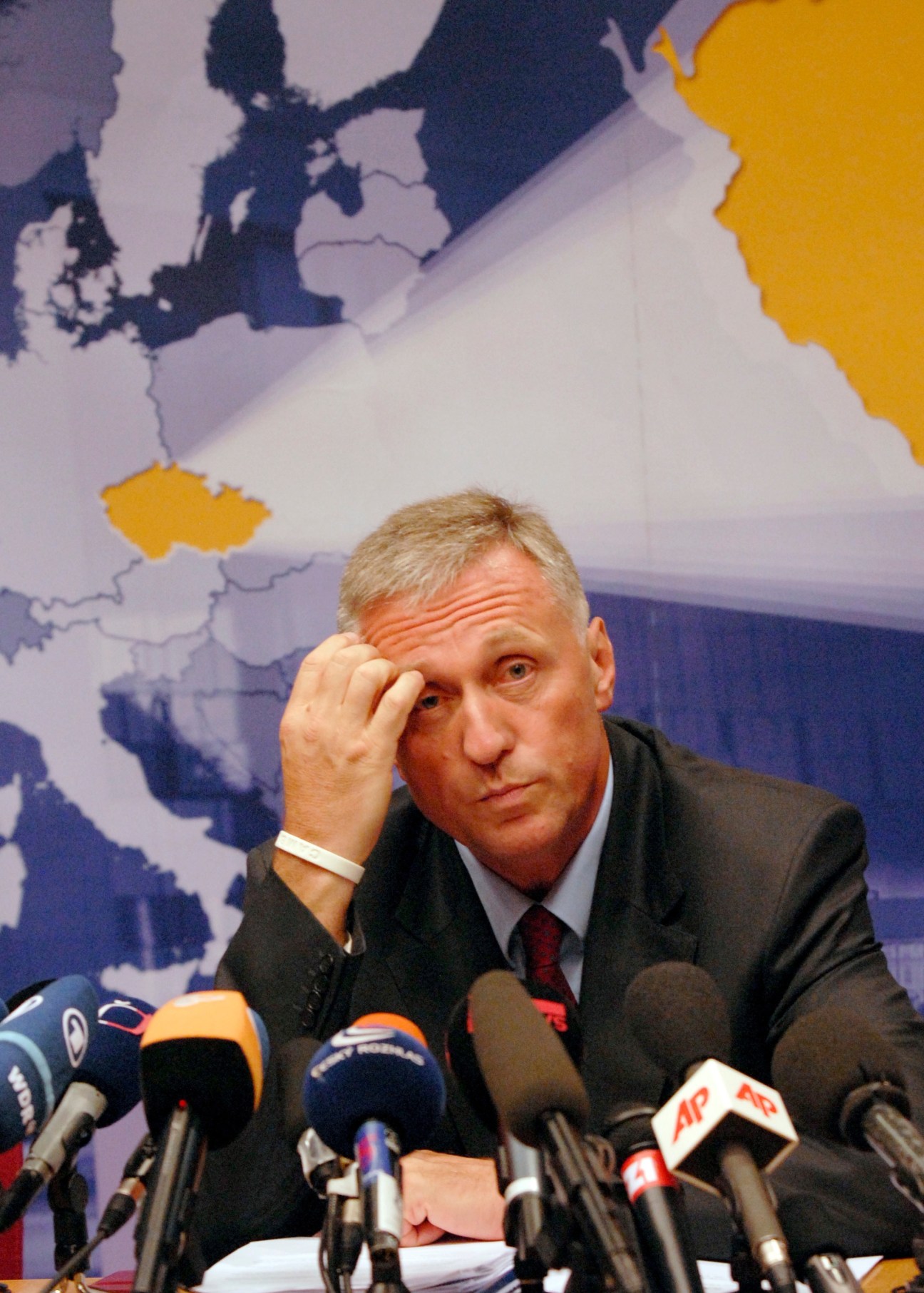 Mirek Topolánek at a press conference with microphones and a European map in the background.