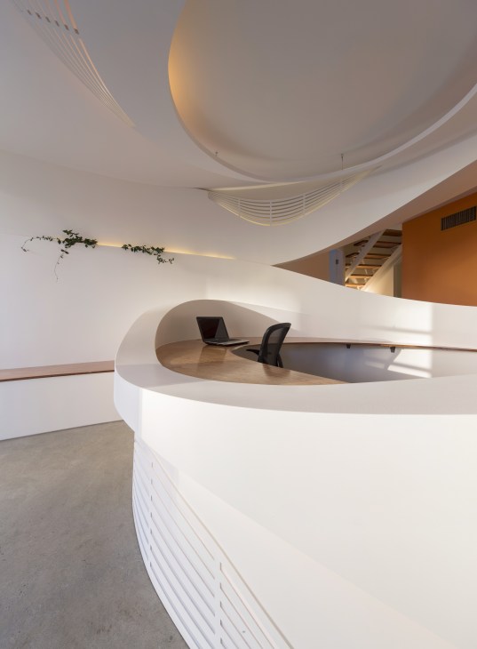 Modern autism centre interior with curved white walls, wooden desk, and sculptural ceiling design.
