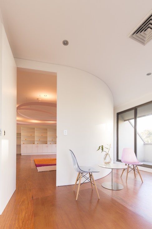Interior of the Edgecliff Medical Centre for Autistic Children in Sydney, featuring a curved white wall, wooden flooring, modern chairs, and warm ambient lighting.