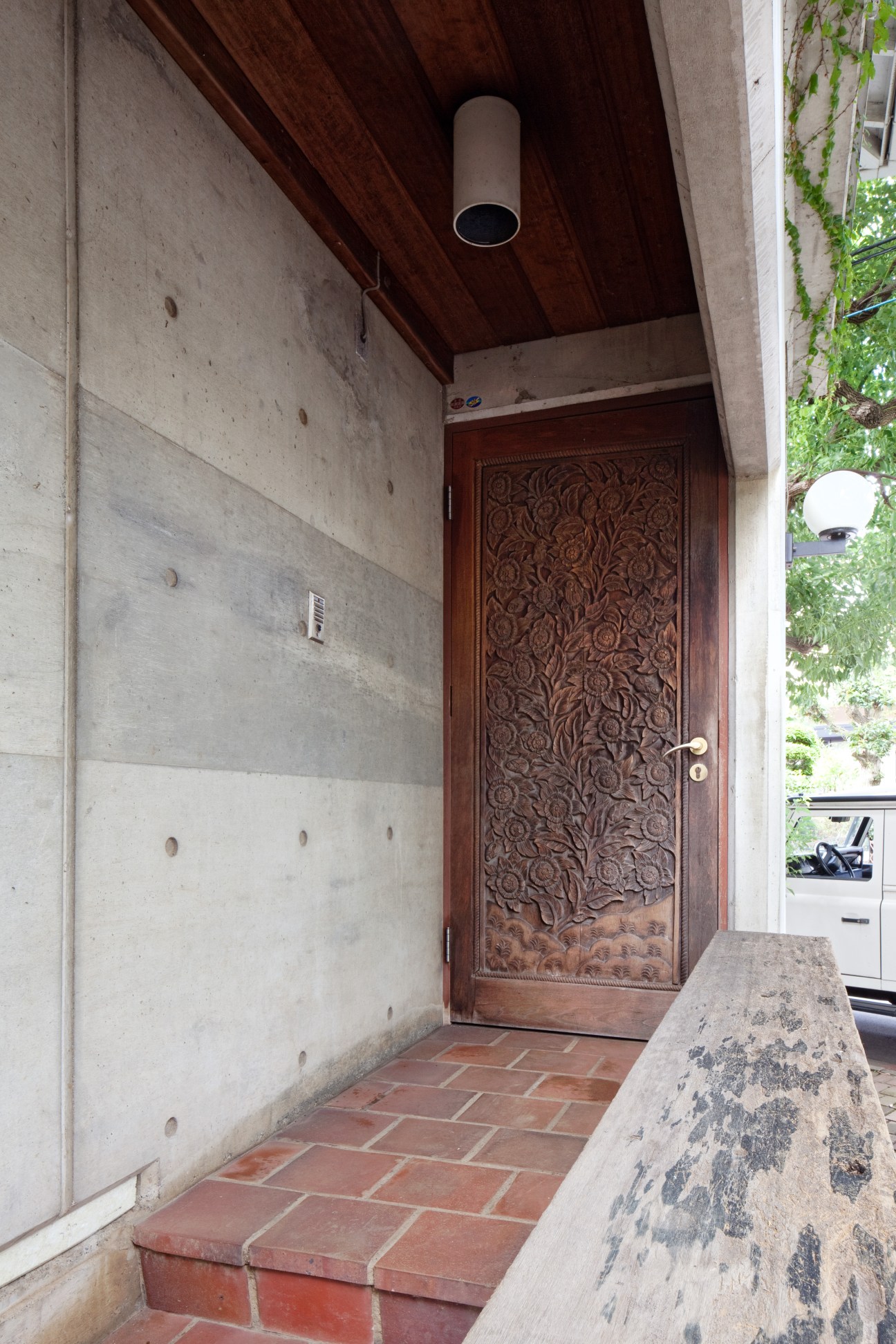 Ornately carved wooden front door with floral motifs under concrete overhang with brick floor