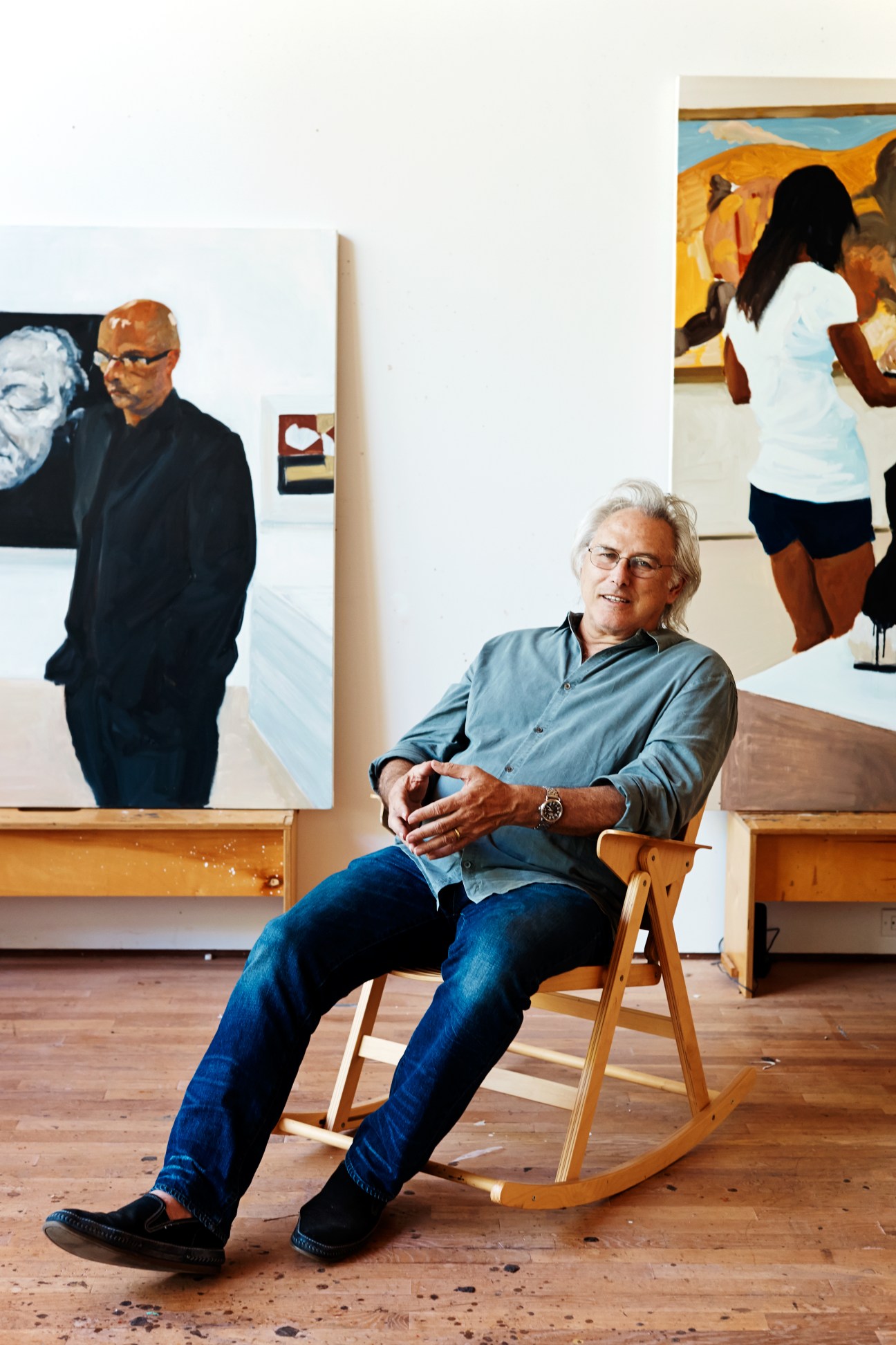 American painter Eric Fischl sits in a rocking chair in his studio surrounded by his figurative paintings.