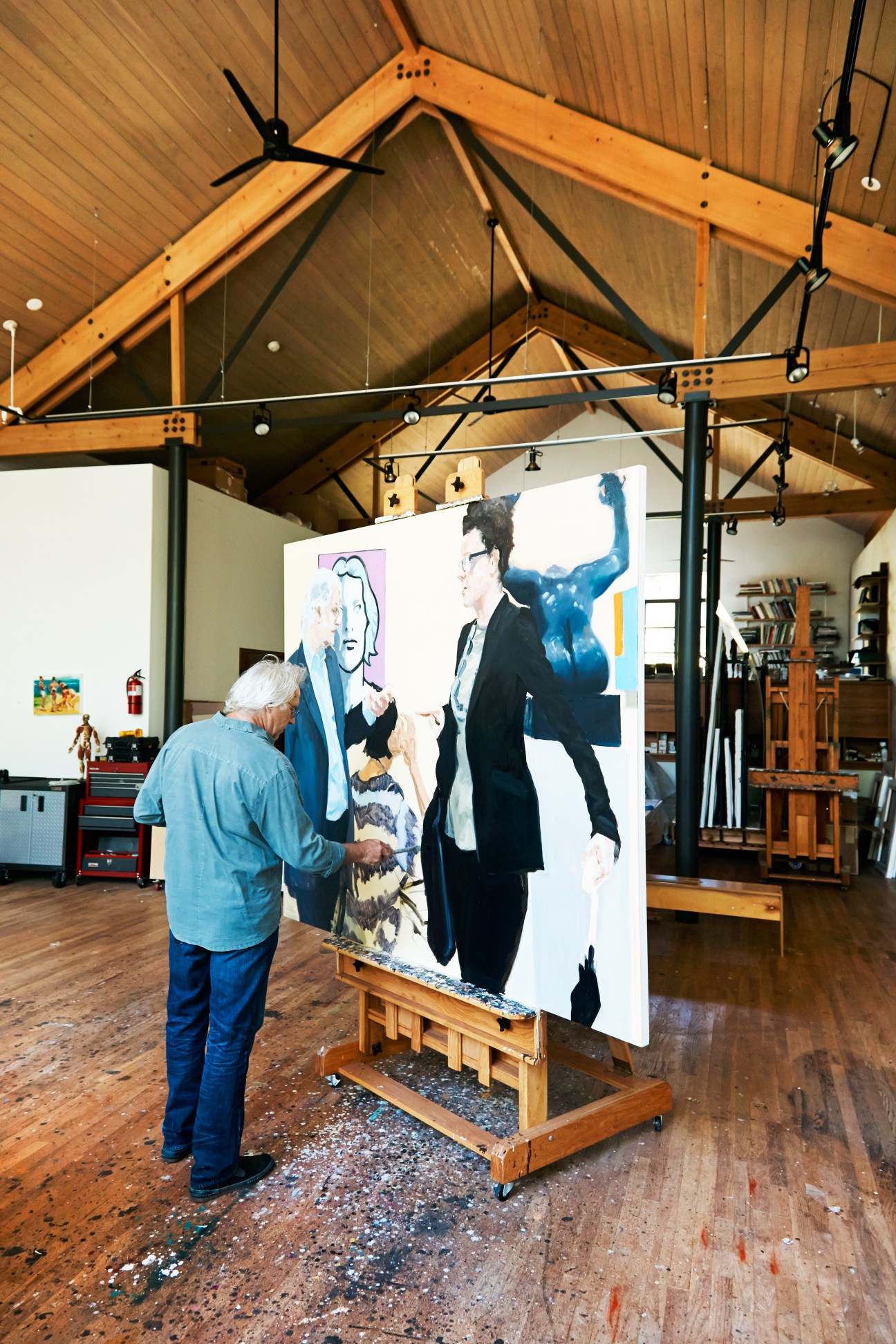 Artist Eric Fischl working on a large canvas in his studio, depicting figures in business attire.