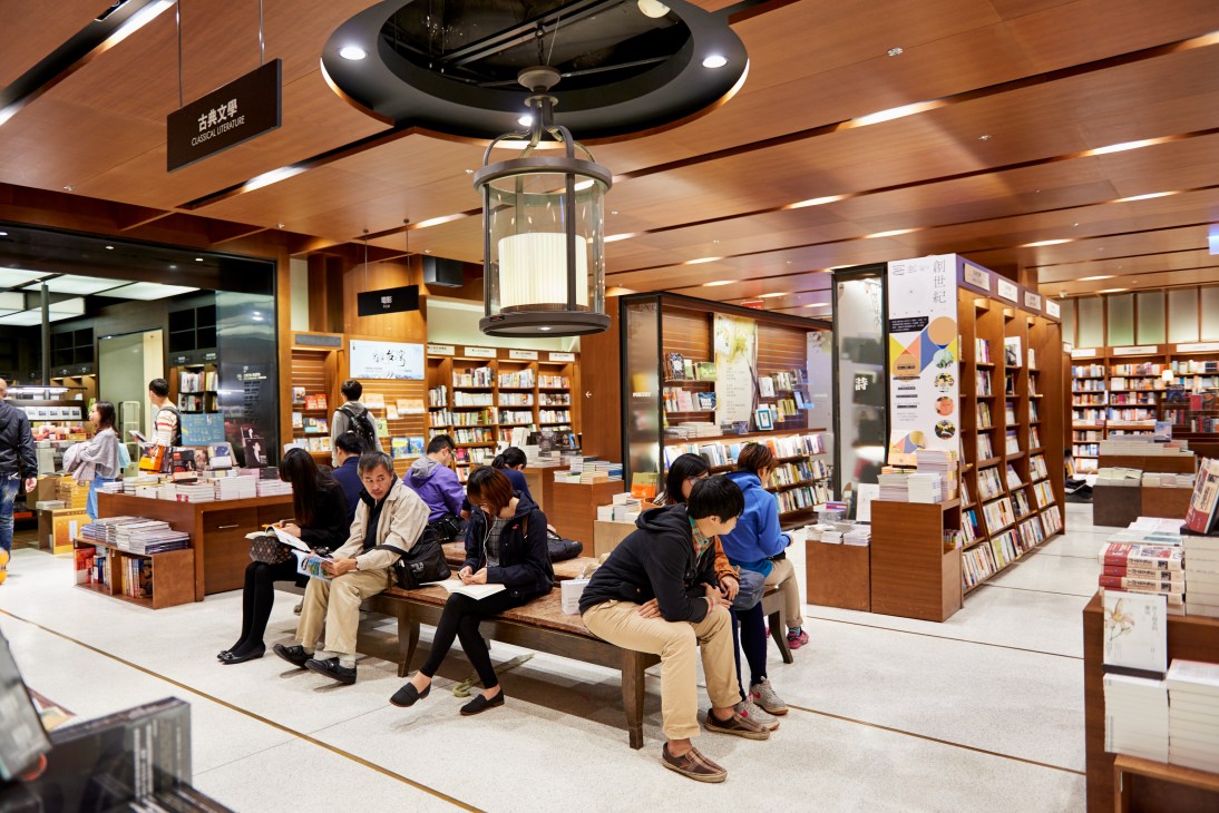 Interior of Eslite bookstore with customers browsing among wooden shelving and seating areas.