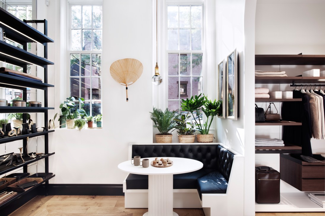 Want Les Essentials retail store interior with black shelving, potted plants, white round table, and black seating.