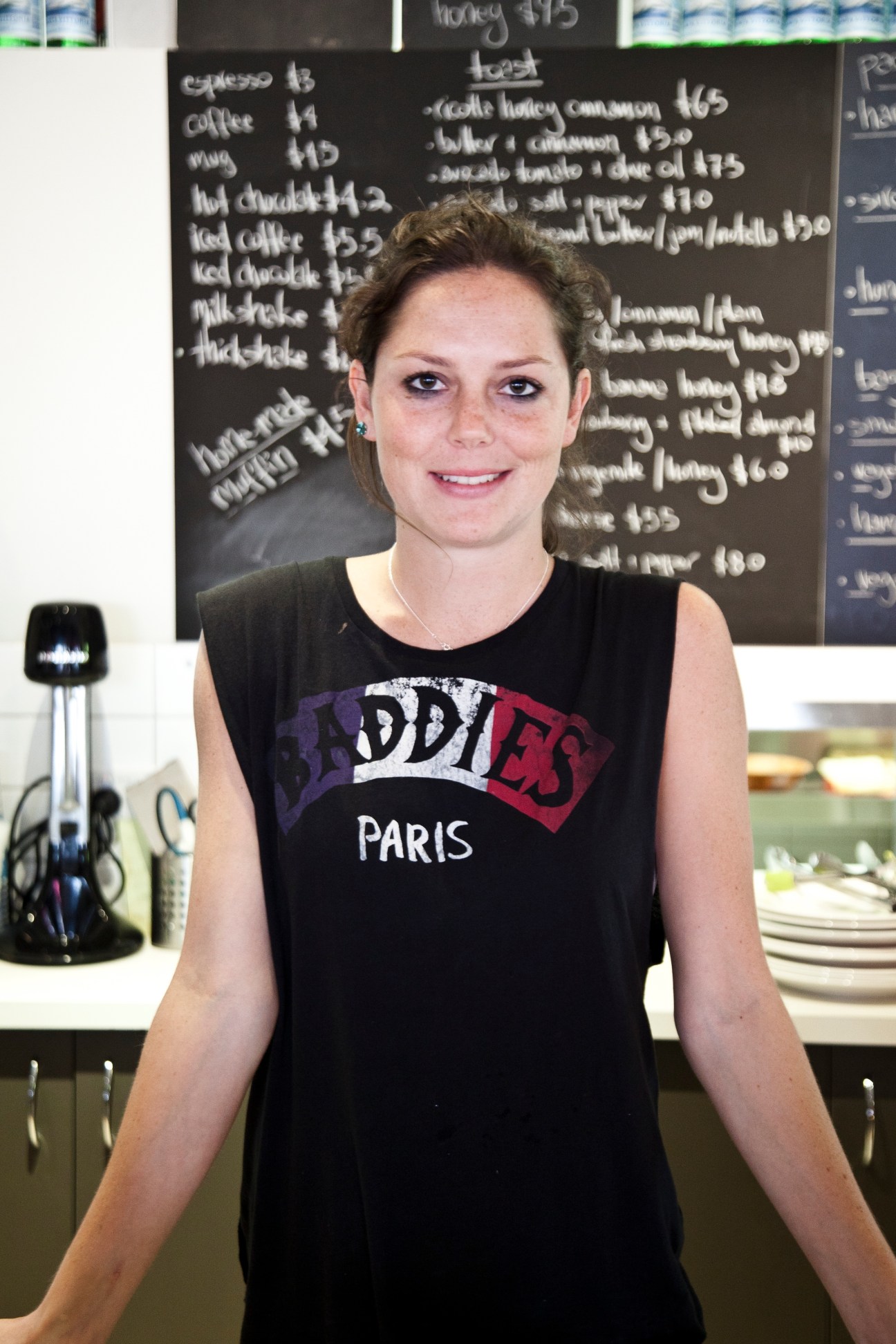 Louisa Ainsworth, owner of Four Birds Cafe, standing in front of a menu board.
