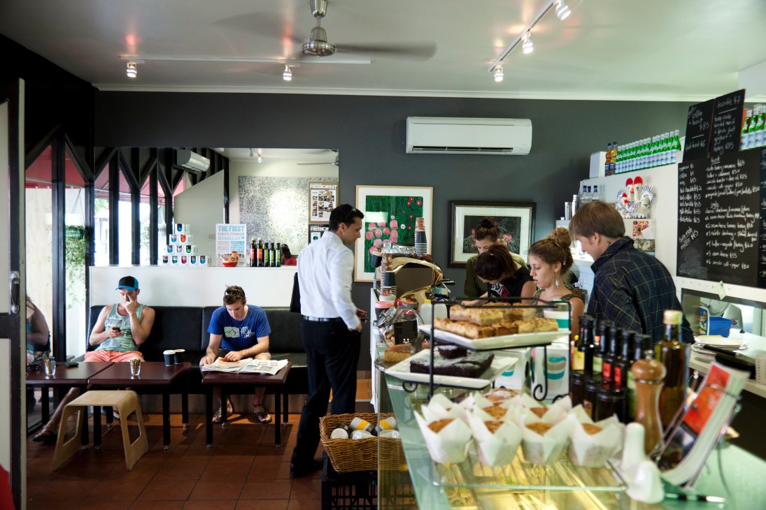 Interior of Four Birds Cafe with customers at counter and seating area with green walls.