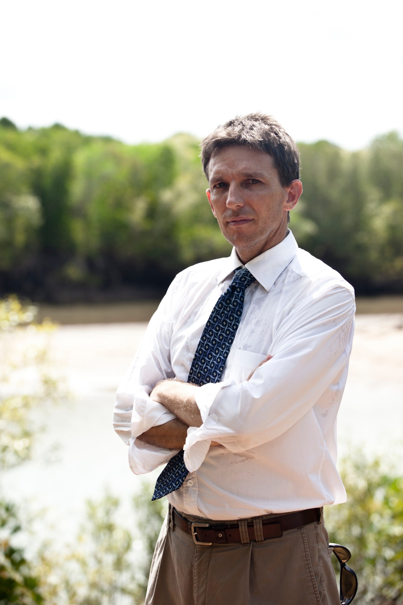 Stuart Blanch, director of the NT Environment Centre, stands with arms crossed by a river with mangrove forests behind him.
