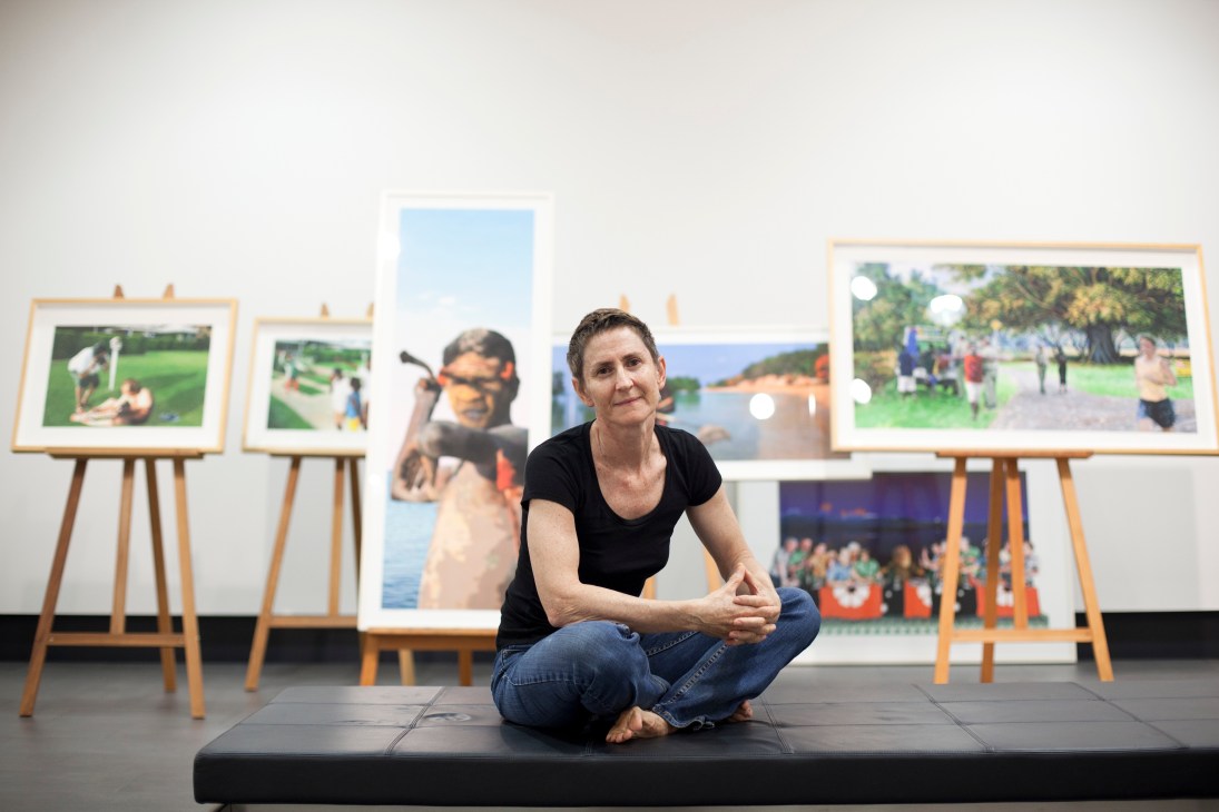 Darwin artist Therese Ritchie crouching in front of her framed landscape and figurative photographs displayed on easels.