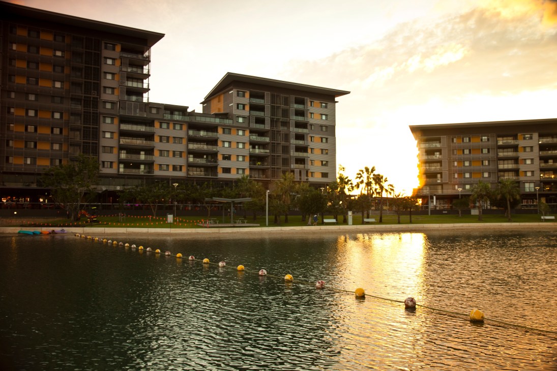 Modern waterfront apartment buildings at sunset with swimming lagoon in foreground.