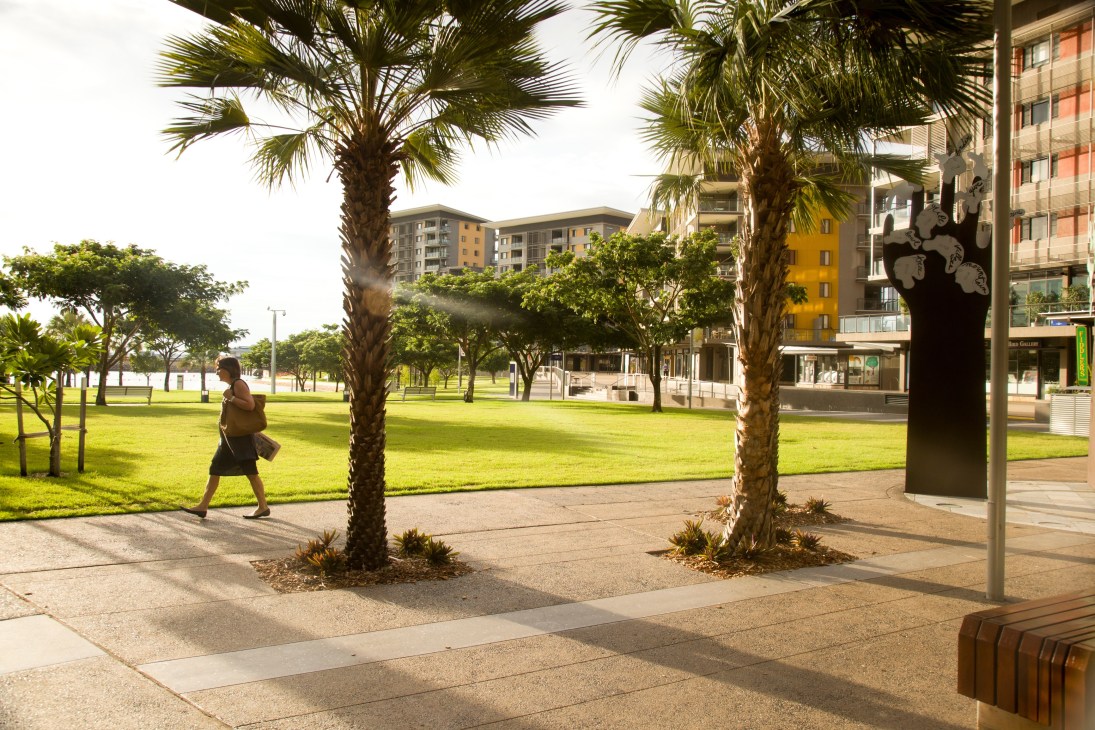 Darwin's Waterfront Precinct with palm trees, manicured lawn, modern apartments and a person jogging.