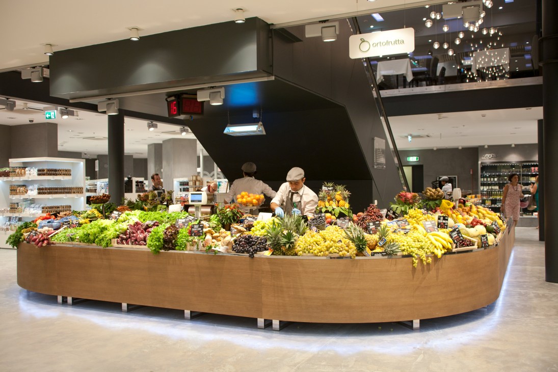 Fresh produce display at Excelsior Milan's food market with colorful fruits and vegetables under modern lighting.