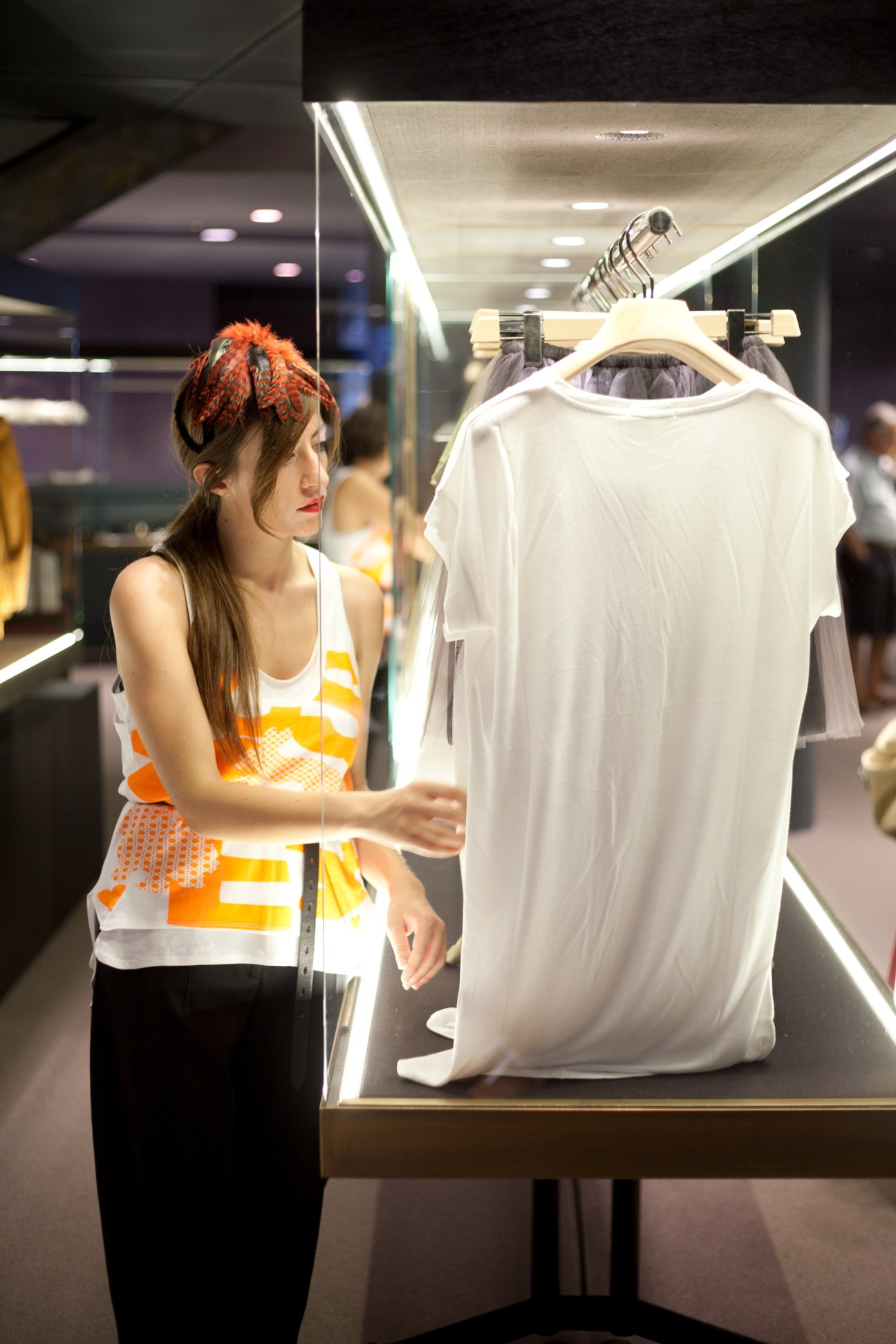 Woman with red hair examining a white garment on display in an illuminated retail window at Excelsior department store.