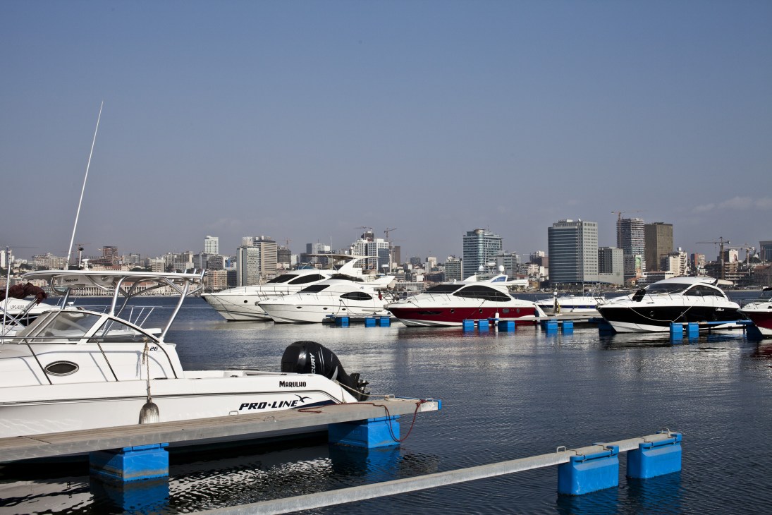 Luxury yachts moored at a marina with Luanda's skyline in the background.