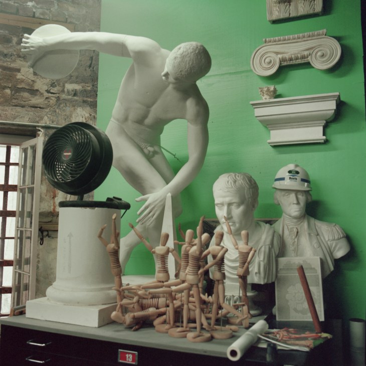 Display of plaster models and sculptures including busts, architectural ornaments, and classical figures against a green wall.
