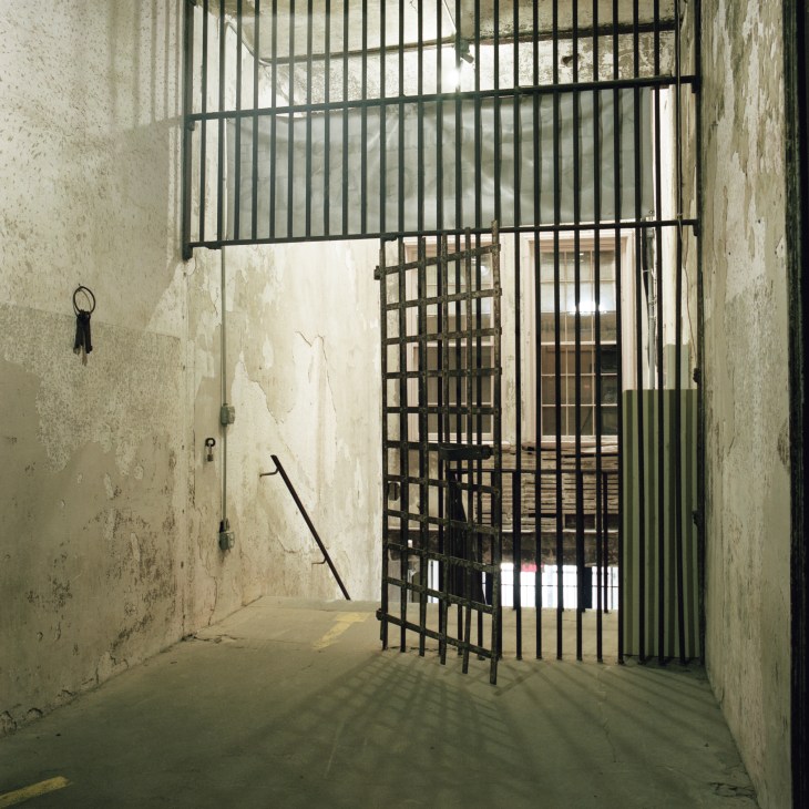 Interior of a historic jail cell with metal bars and weathered concrete walls.