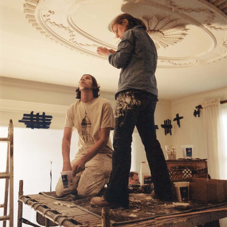 Two plaster workers applying decorative ceiling details in a Georgian Revival townhouse interior.