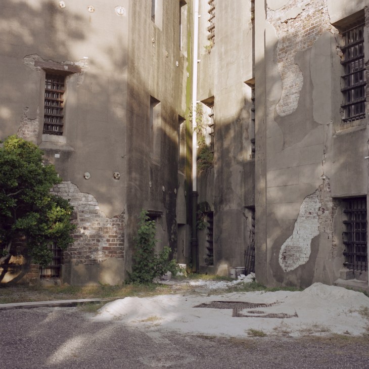 Interior courtyard of the Old Charleston Jail showing deteriorating brick and stone walls with barred windows and overgrown vegetation.