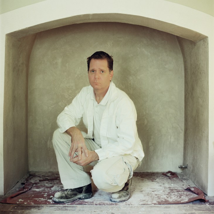 Man in white shirt crouching in an arched alcove with plaster walls.