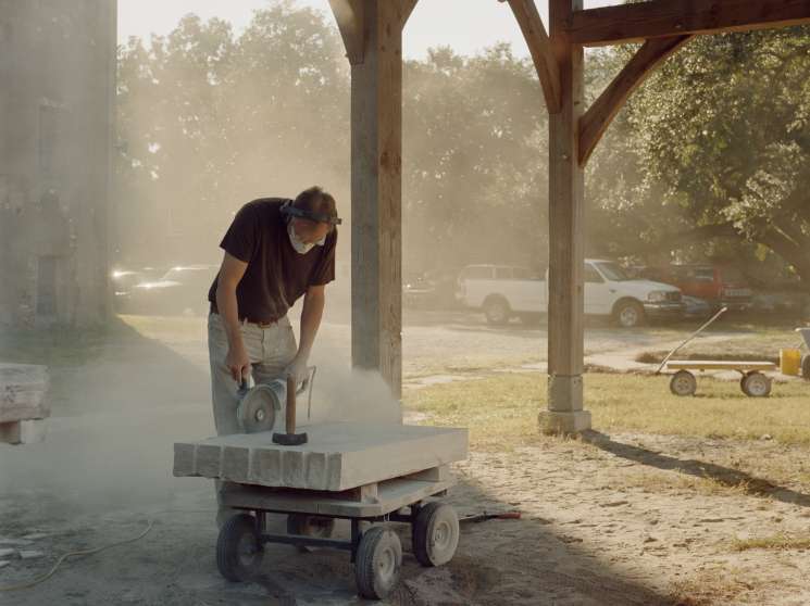 Simeon Warren, dean of the college, carving stone at an outdoor workshop under a wooden structure.