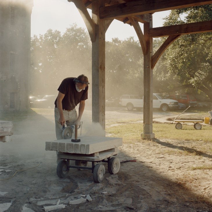 Simeon Warren, dean of the college, carving stone at an outdoor workshop under a wooden structure.