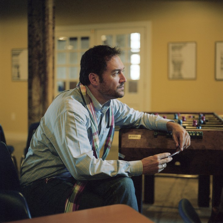 William H Bates, professor of architecture and design, sits in a yellow room holding architectural plans.