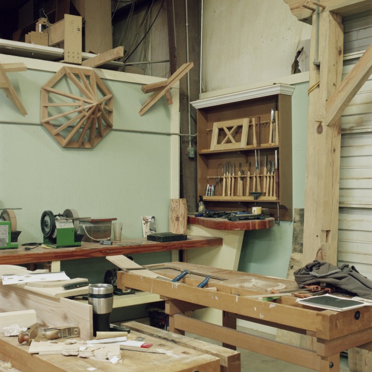 Carpentry workshop with wooden workbenches, hand tools, and geometric wooden models on pale green walls.