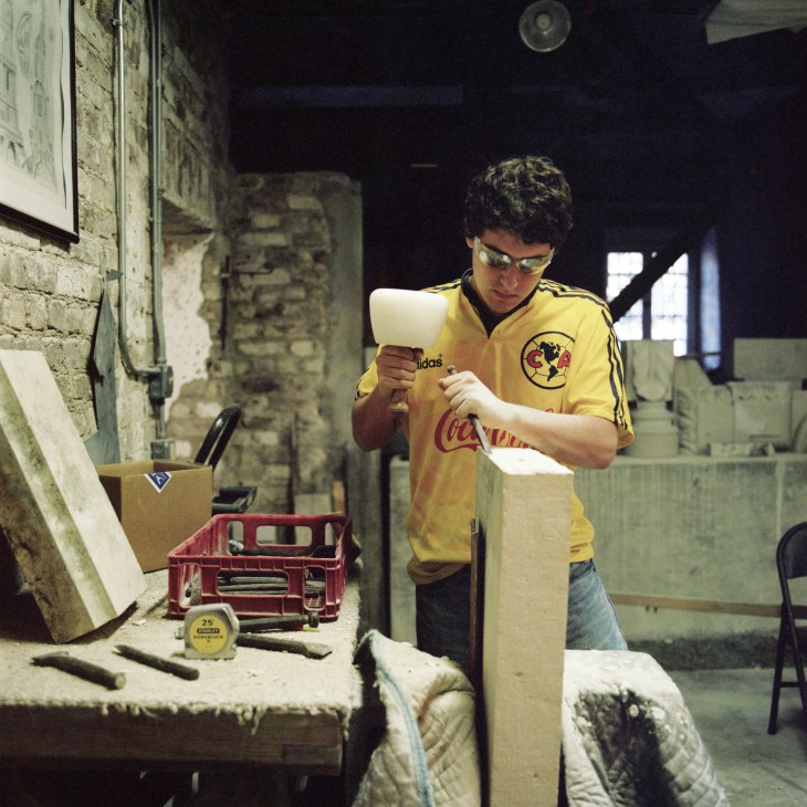 Student in yellow Adidas jacket carving stone with chisel and mallet in workshop