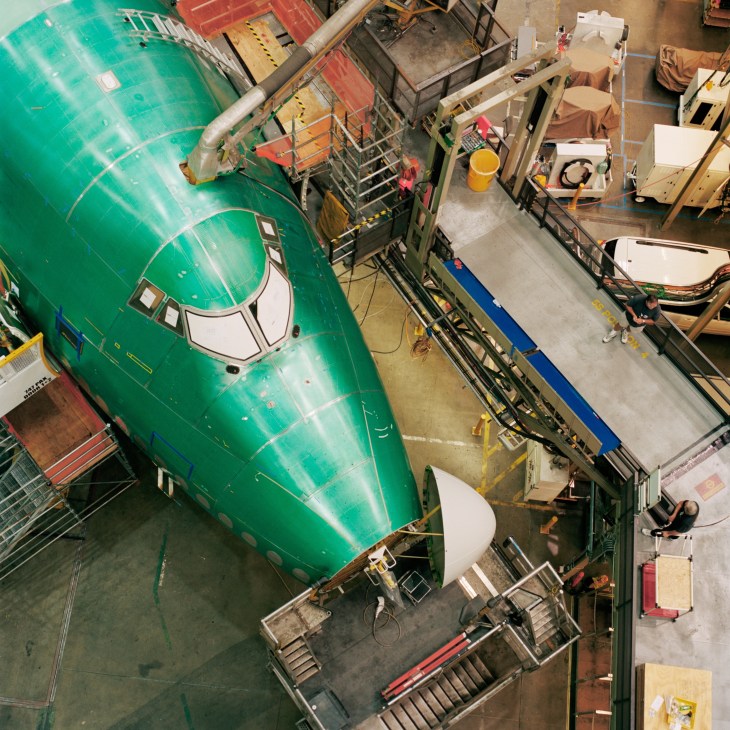 Overhead view of Boeing 747-8 nose section in green livery during assembly at Everett factory with workers and equipment surrounding it.