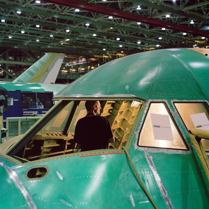 Worker assembling interior components inside the cockpit of a Boeing 747-8 under factory lights.