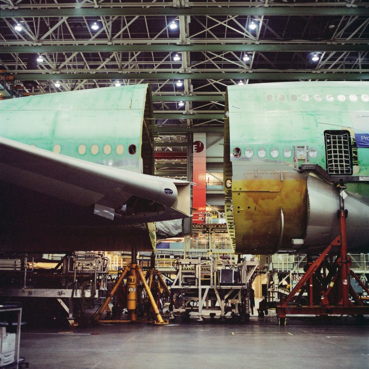 Front and middle sections of a Boeing 747-8 aircraft under assembly in a factory hangar.