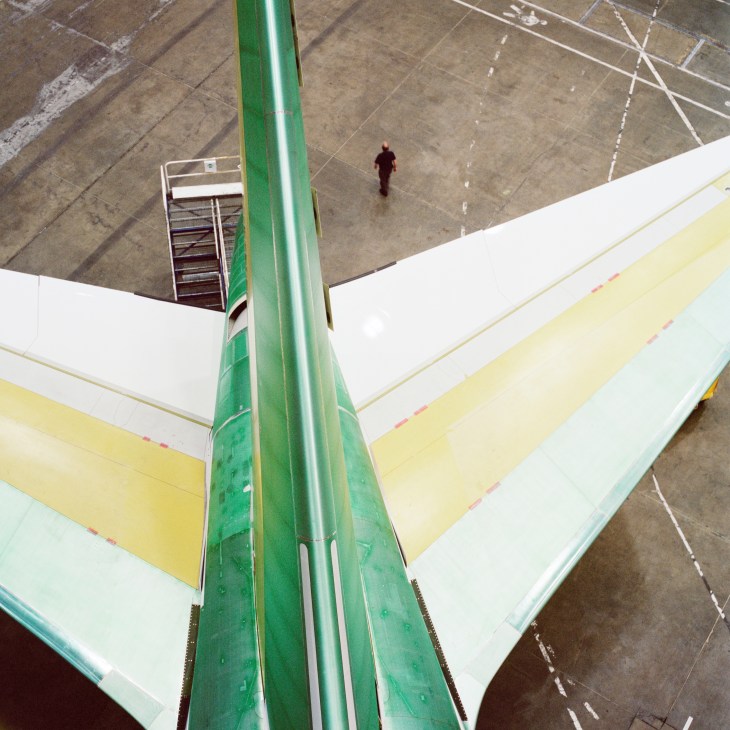Aerial view of a Boeing 747-8 tailplane with green structural support and white fuselage sections in an assembly hangar.