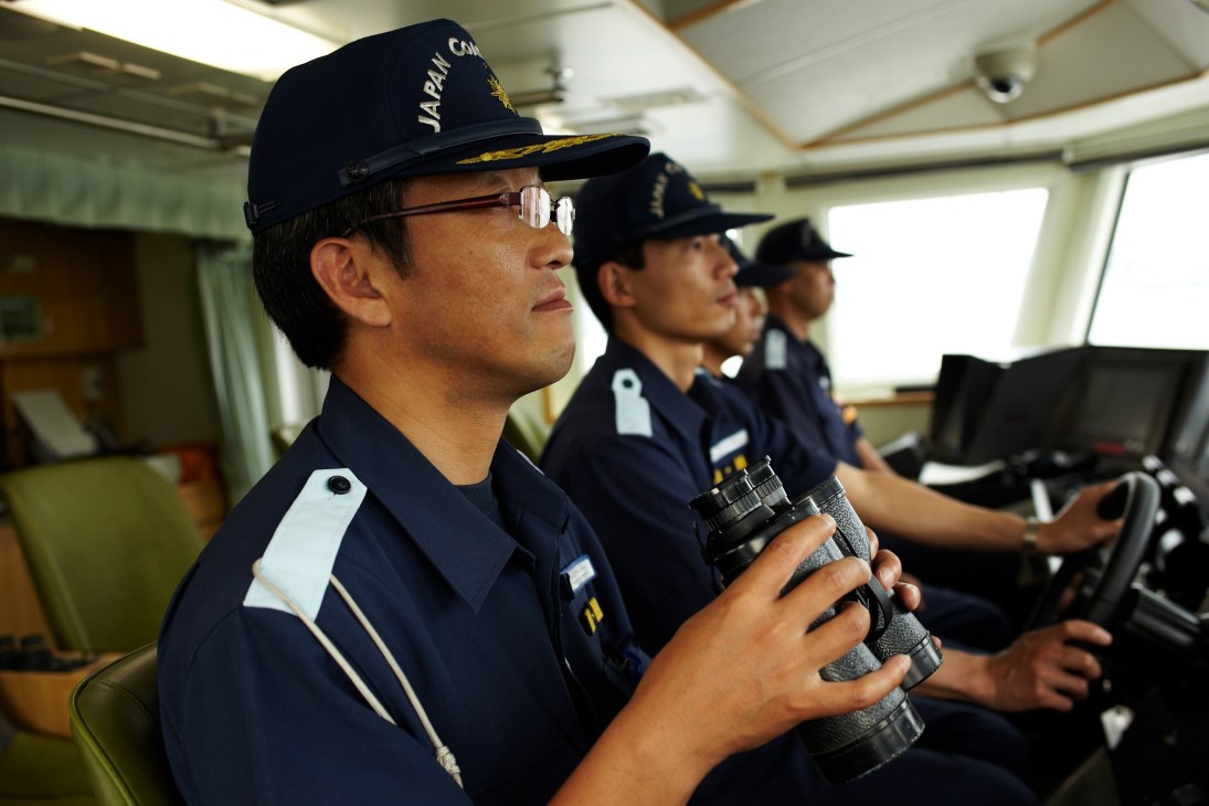 JCG officers in uniform on board a patrol vessel holding binoculars.