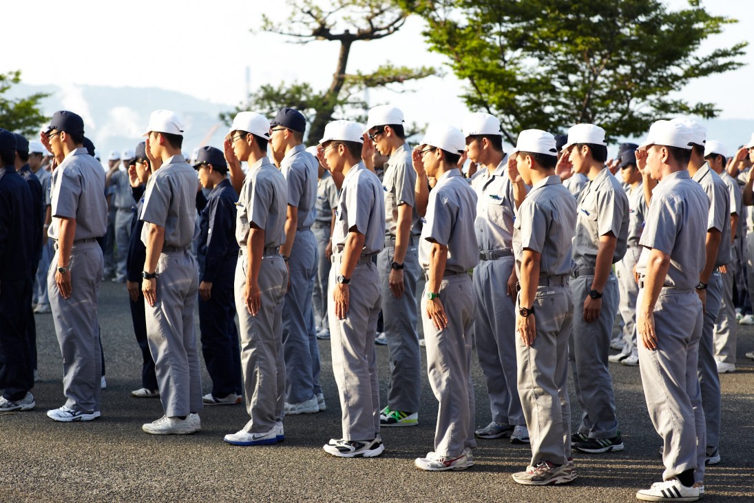 Japan Coast Guard officers in uniform and white caps standing in formation during morning exercise salute.