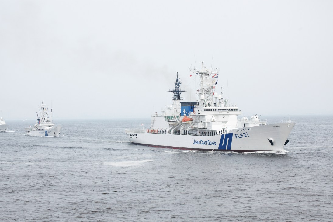 Two Japan Coast Guard patrol vessels at sea, with personnel lined up on deck during a fleet viewing event.