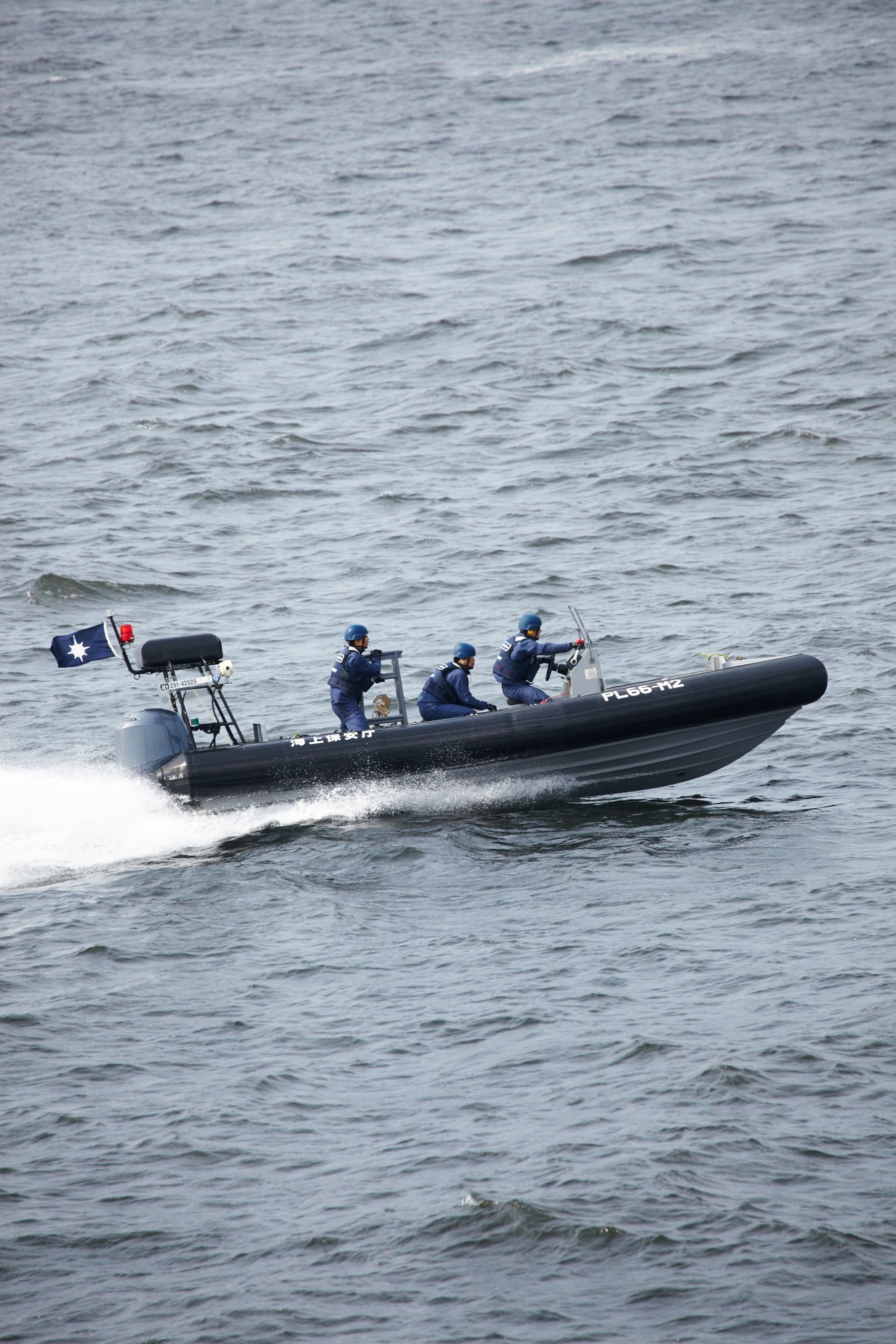 Japan Coast Guard officers in a speedboat conducting pursuit training exercise on open water.