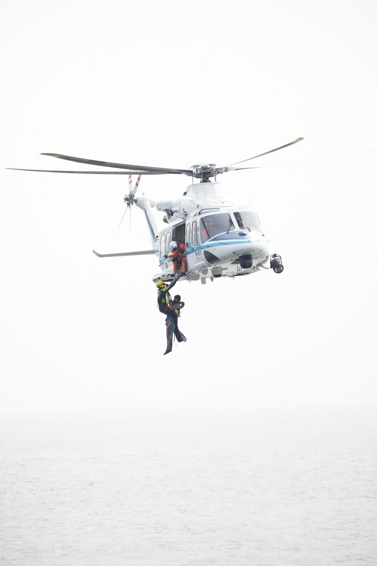 JCG helicopter performing a hoist-rescue demonstration with a person being lifted from the water below.