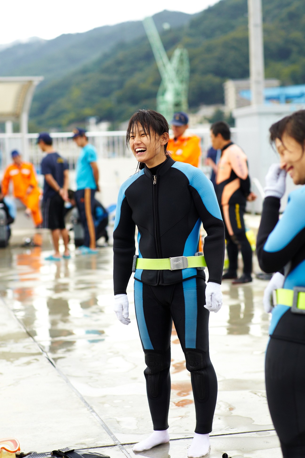 JCG academy student in wetsuit smiling after training session with other trainees in background.