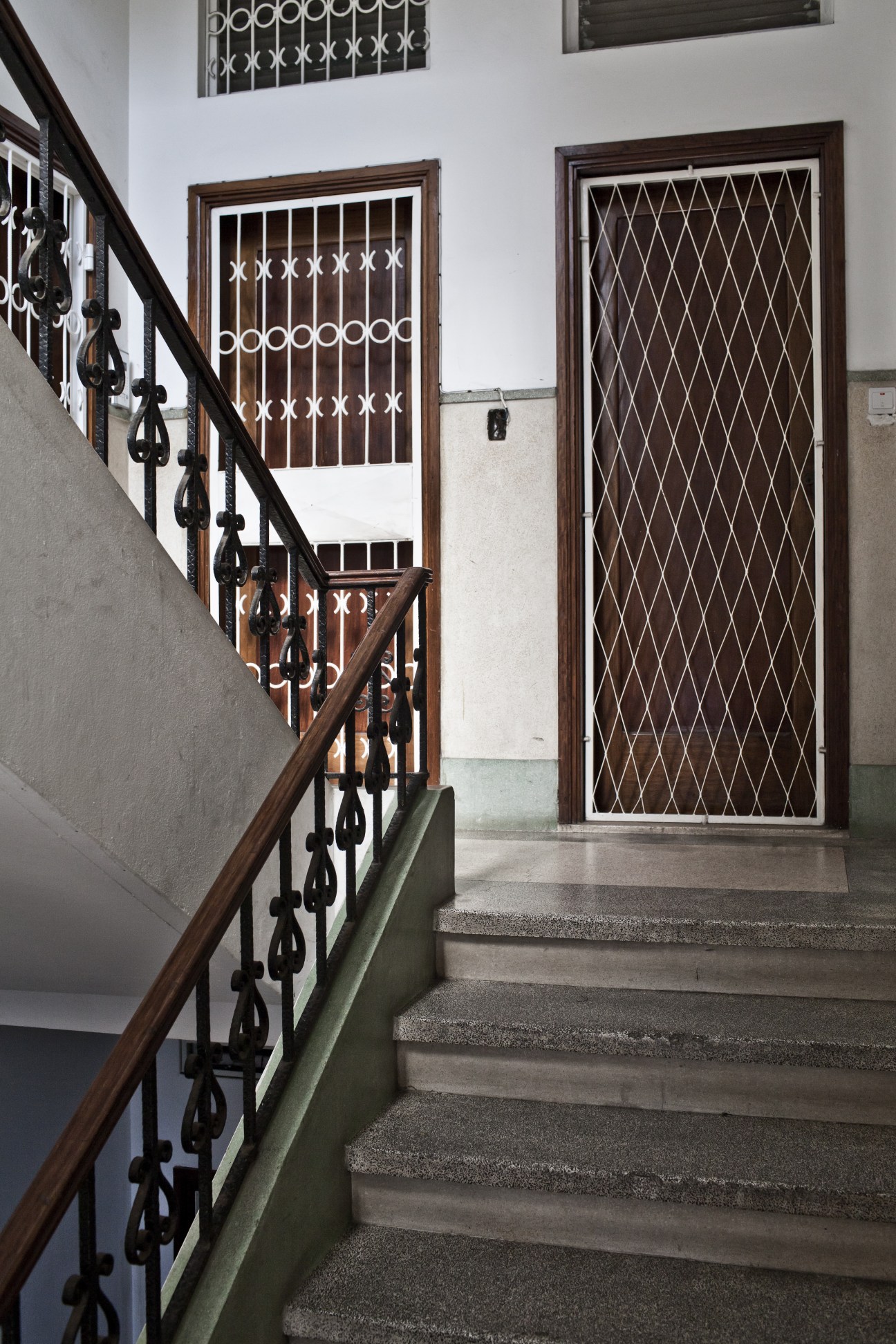Staircase in a 1950s modernist apartment block with wooden railings and decorative metal gates.