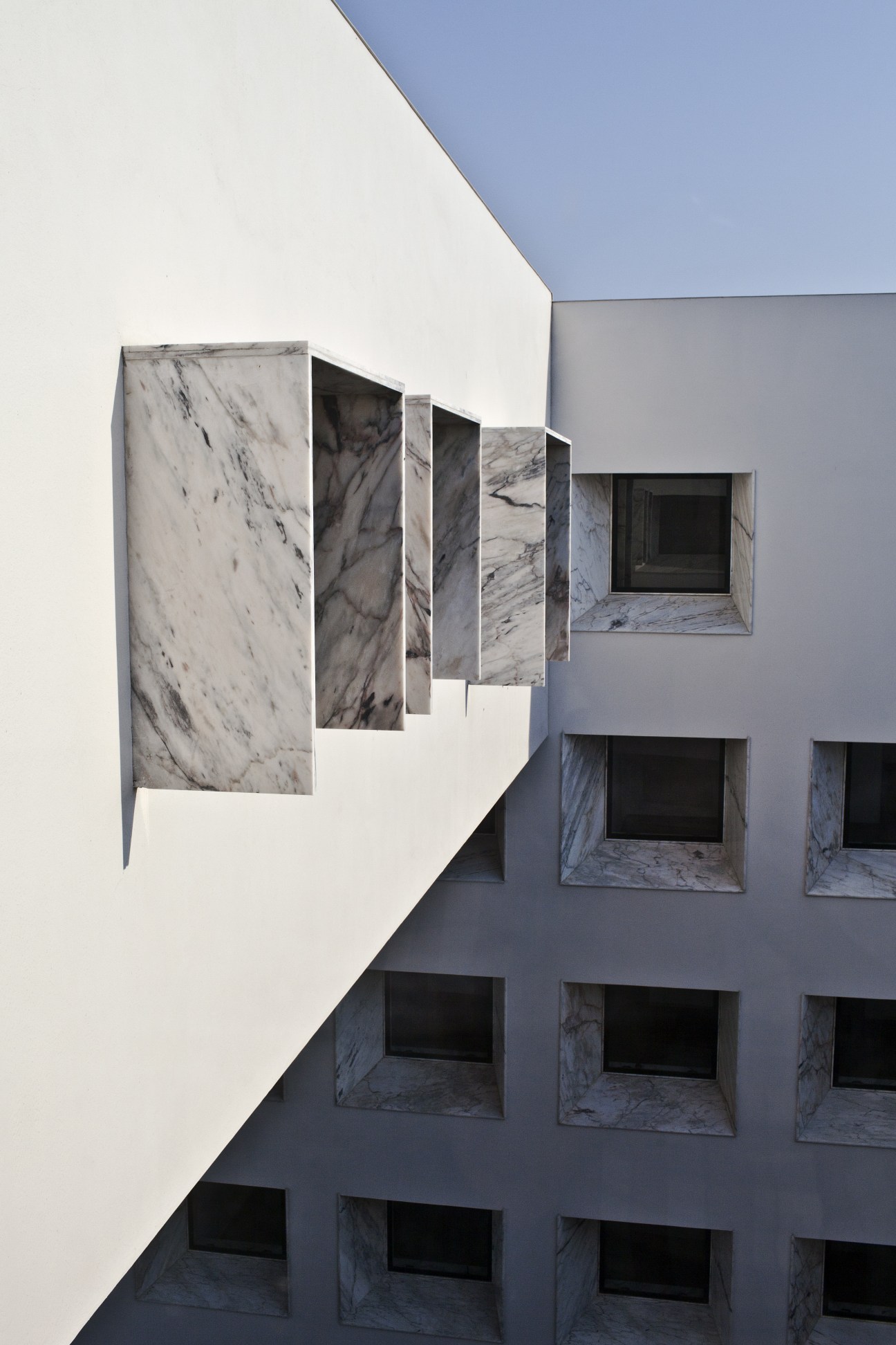 White marble and concrete modern building facade with geometric window openings and decorative marble panel details.