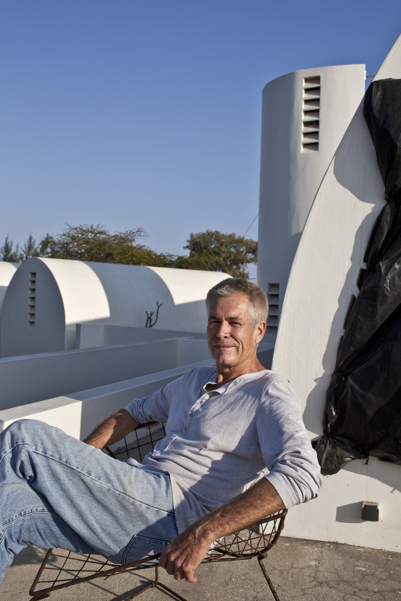 Fion de Vletler sits on a chair in front of his modernist white concrete house designed by architect José Forjaz.