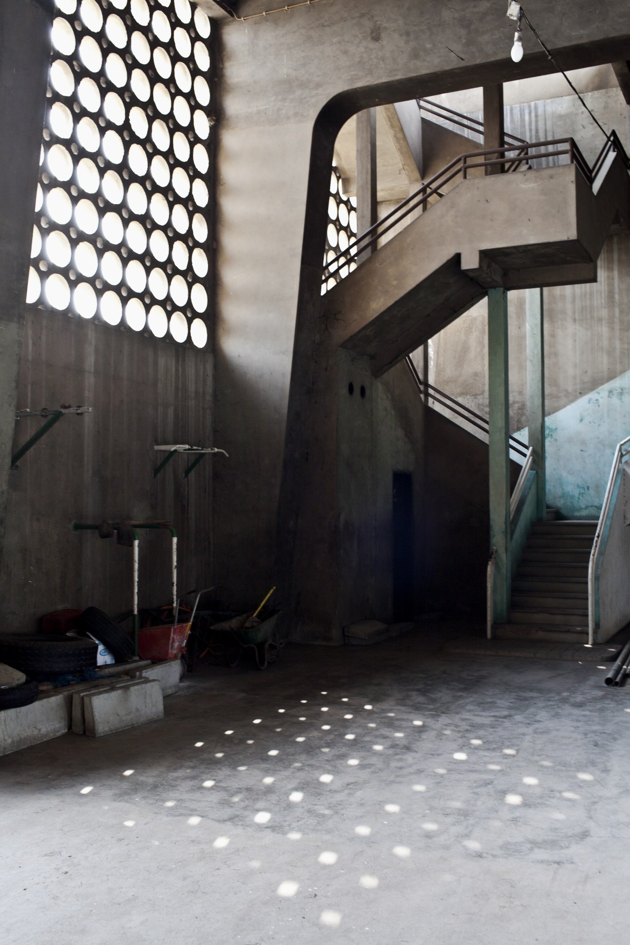 Interior of modernist concrete structure with circular perforated wall panel and curved spiral staircase.