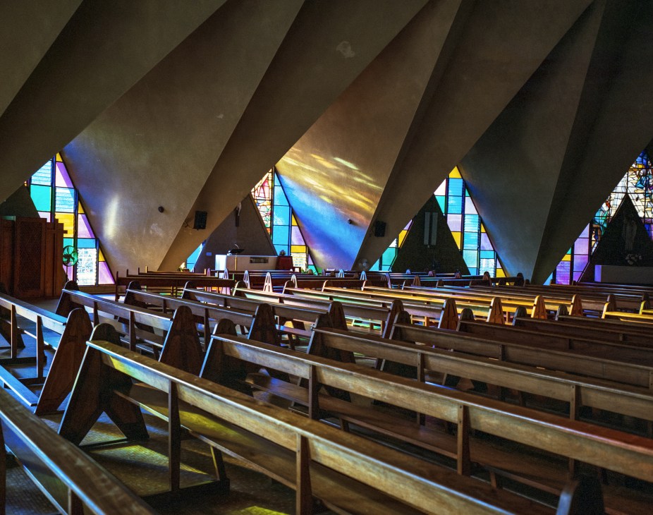 Interior of St Antonio church with angled concrete ceiling beams and colorful stained glass windows.