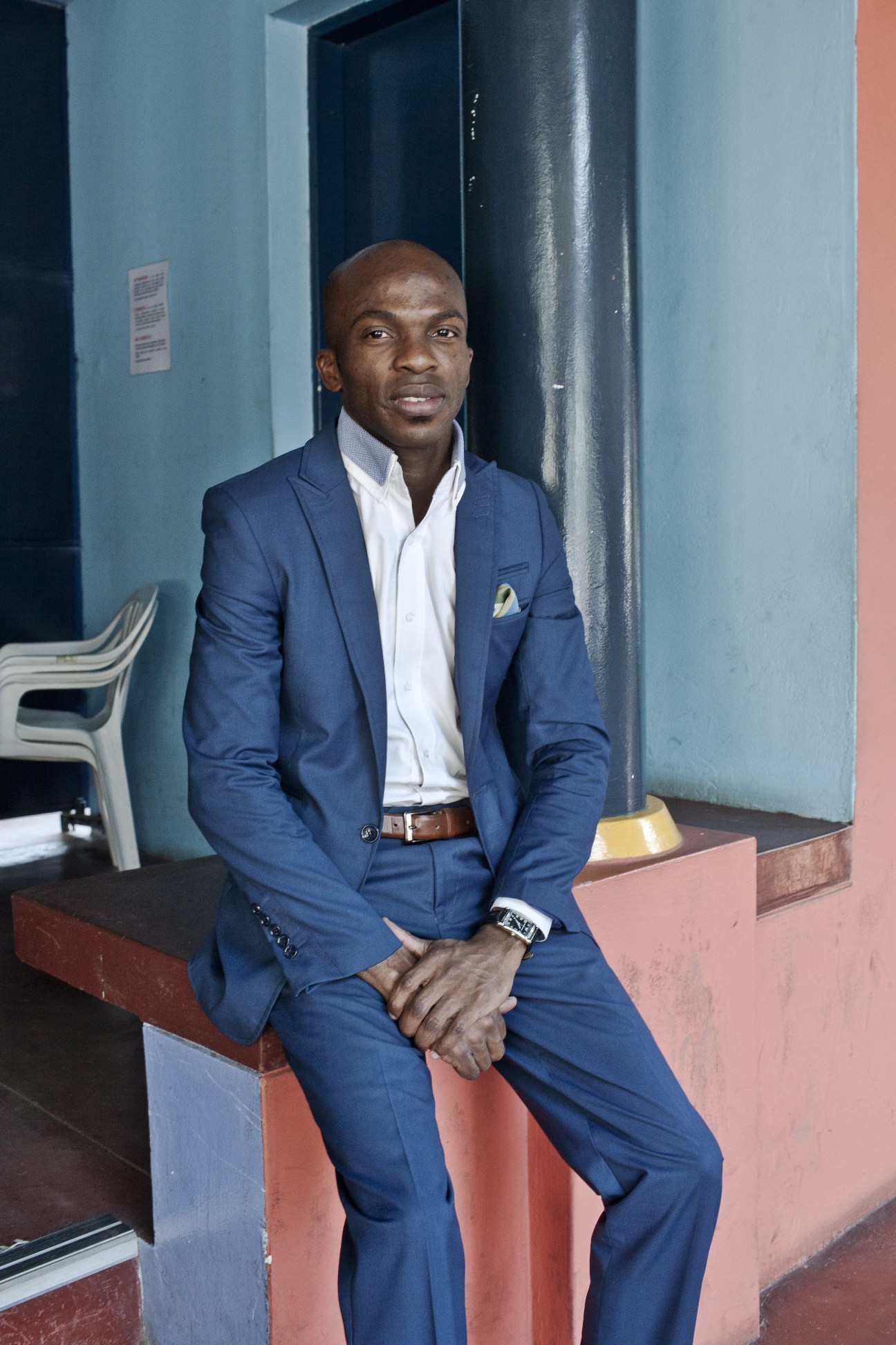 Poet Paco Sininho sitting on a colorful modernist bench in a blue suit.