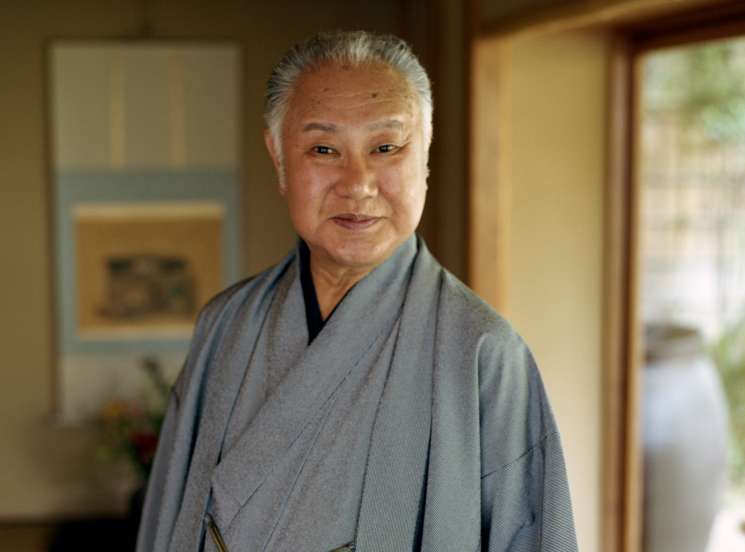 Tojuro Sakata, an elderly kabuki actor, wears a grey kimono with gold embroidered details in a traditional Japanese interior.