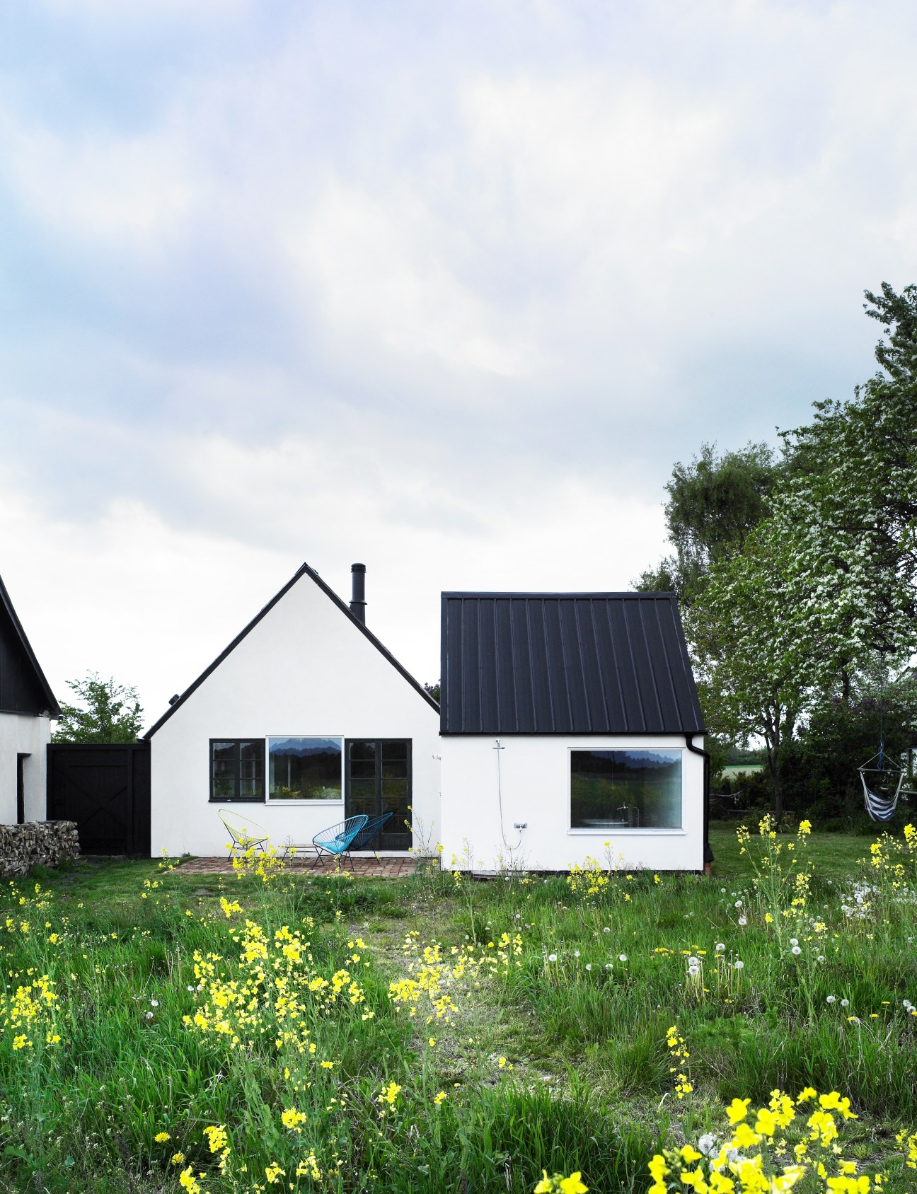 Modern white summer holiday home with dark roof designed by LASC studio in Copenhagen surrounded by wildflowers.