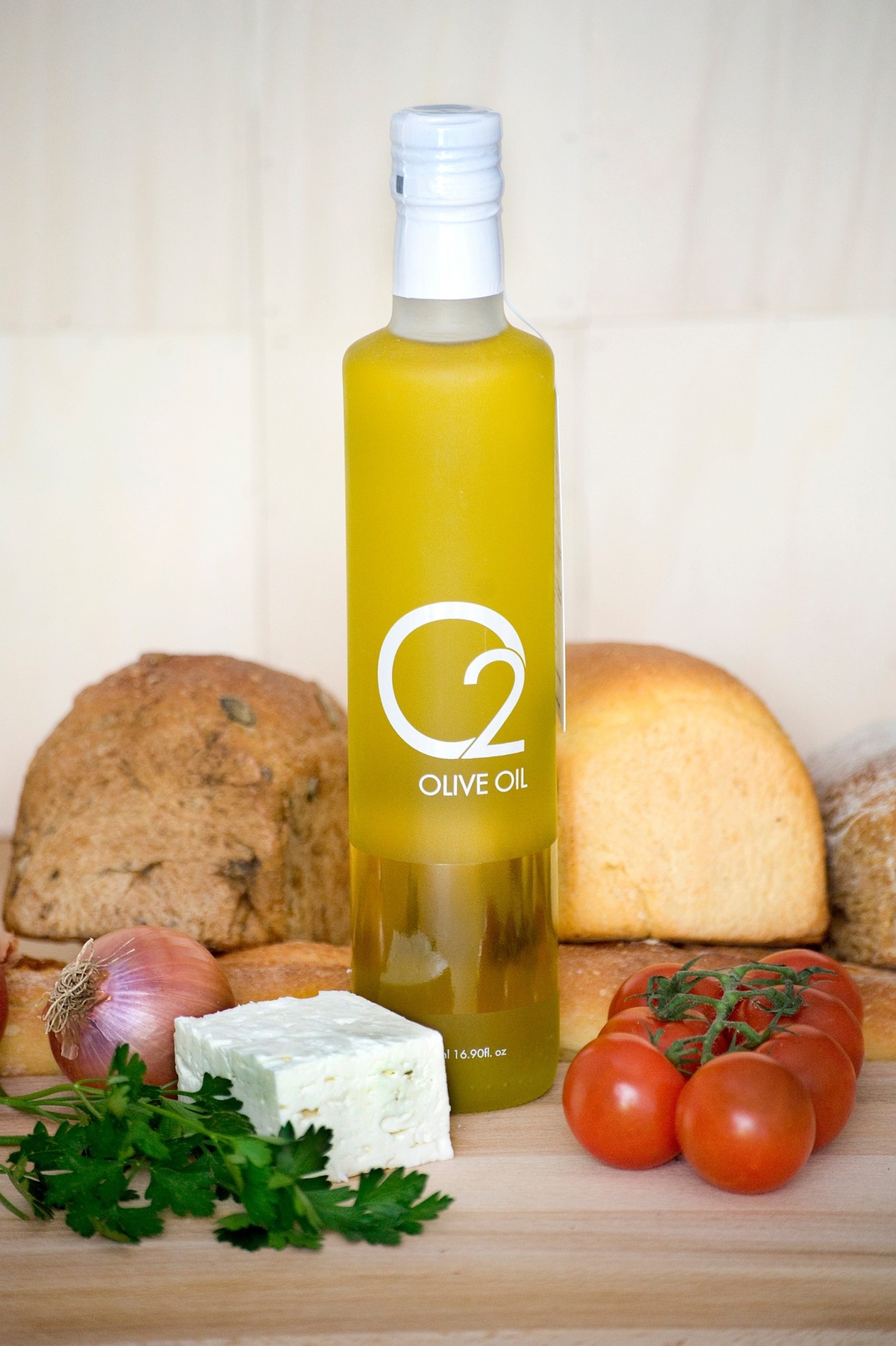 O2 Olive Oil bottle surrounded by bread, cheese, tomatoes, onion and parsley.
